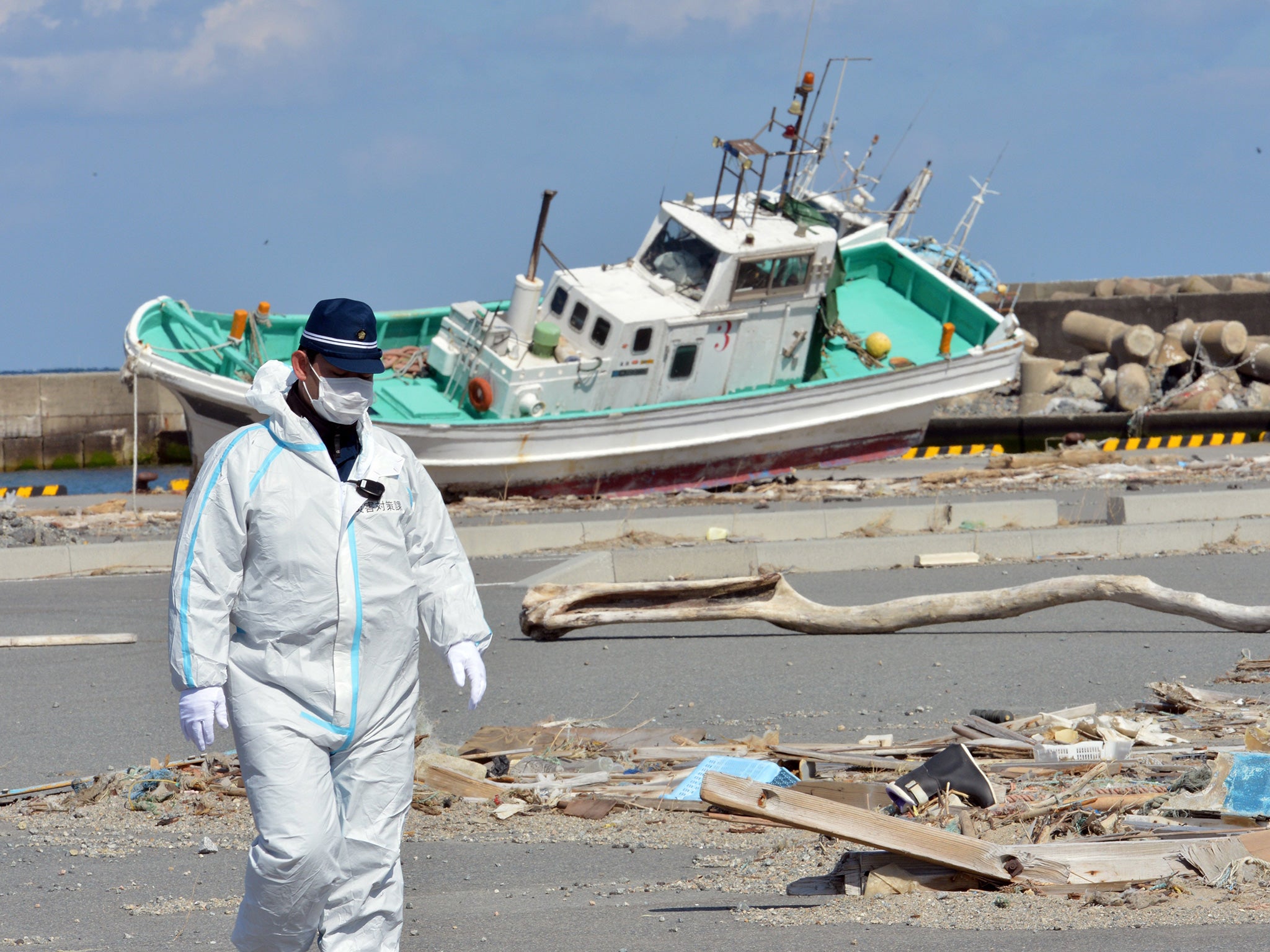 A police officer walks on a pier to search for missing people as a wrecked ship (back) still rests grounded in Namie, near the striken TEPCO's Fukushima Dai-ichi nuclear plant