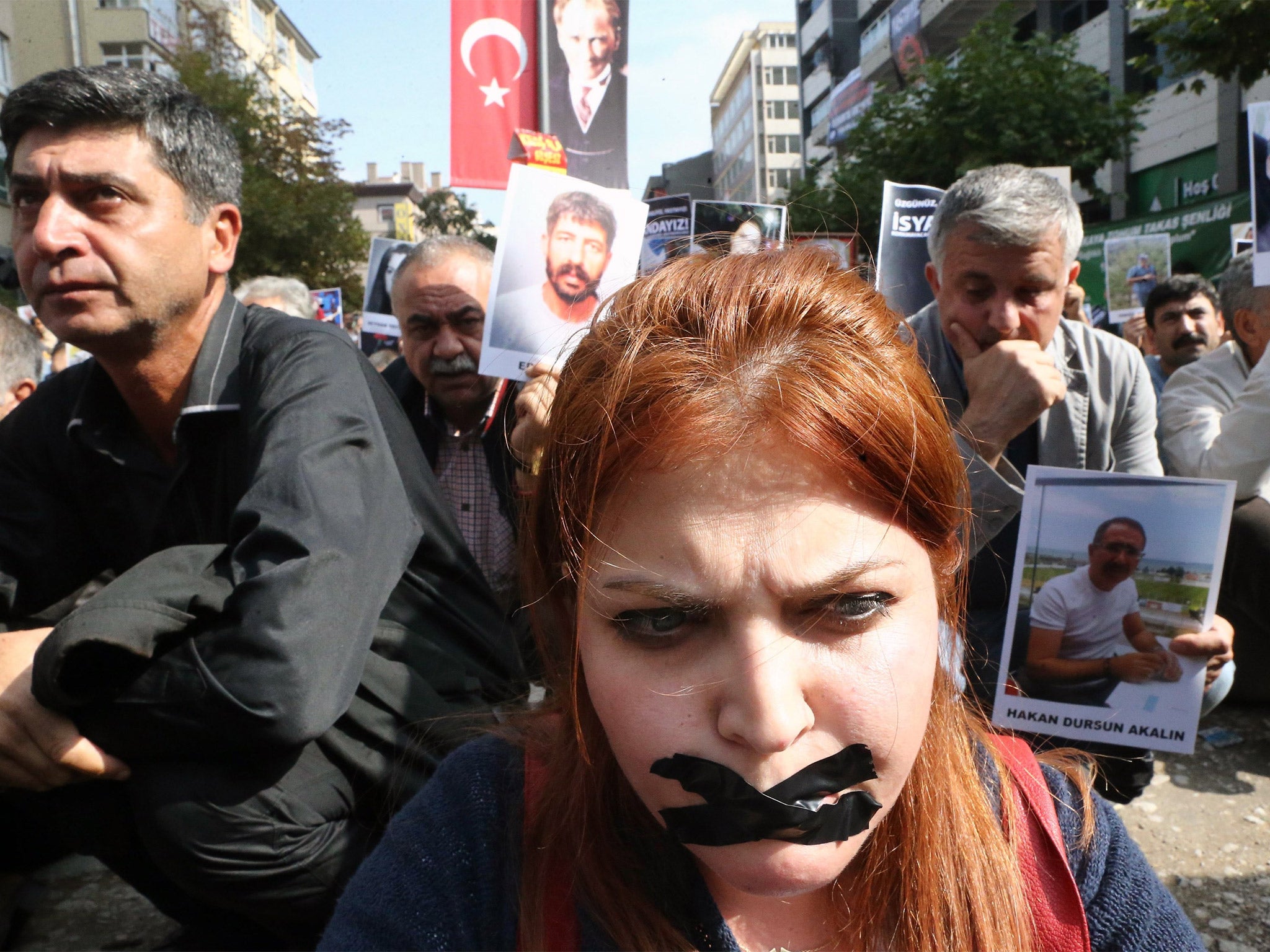 A demonstrator wears tape on her mouth as others hold portraits of people killed by suicide bombings as they attend a commemoration in Ankara (Getty)
