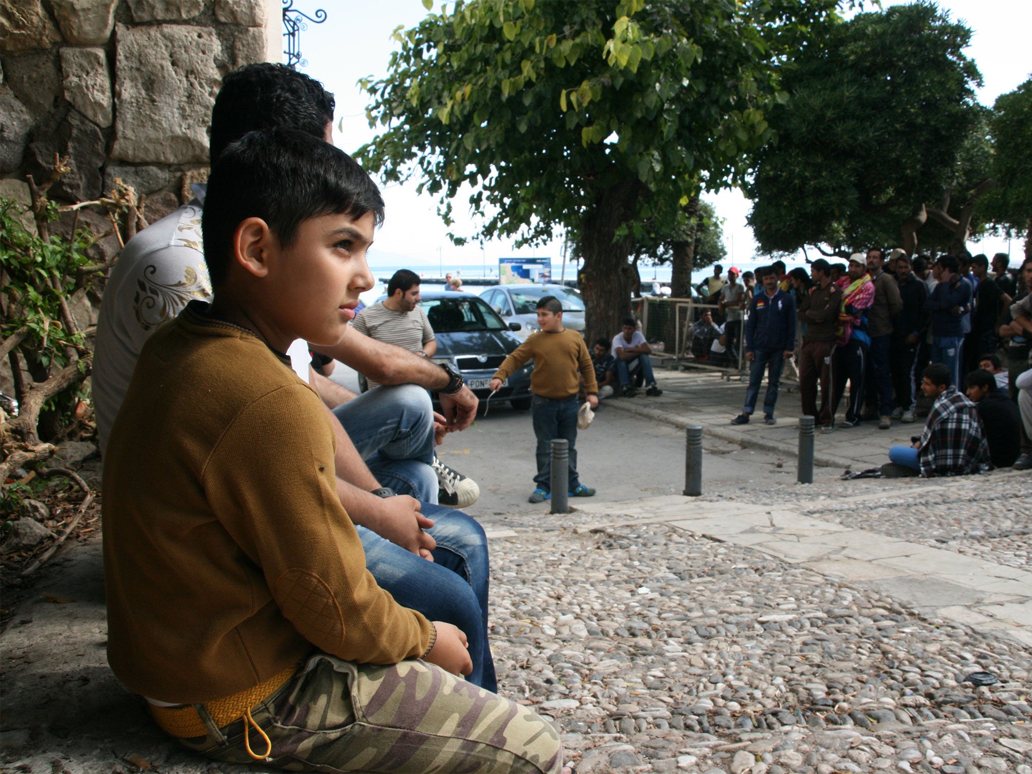 &#13;
A young Pakistani and his family wait on the curb outside the downtown Kos police station where refugees must register upon arrival on the island (Photo by Cody Punter)&#13;