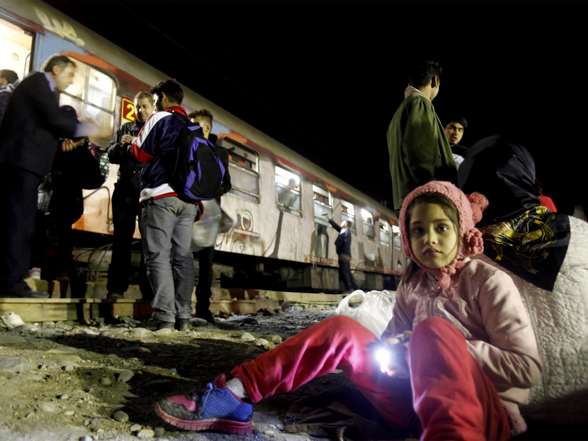 A refugee girl holds a flashlight awaiting with her family to board a train heading towards Bulgaria