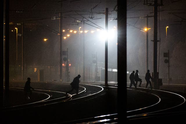 People walk across train tracks near the Eurotunnel terminal in Coquelles on August 3, 2015 in Calais, France.