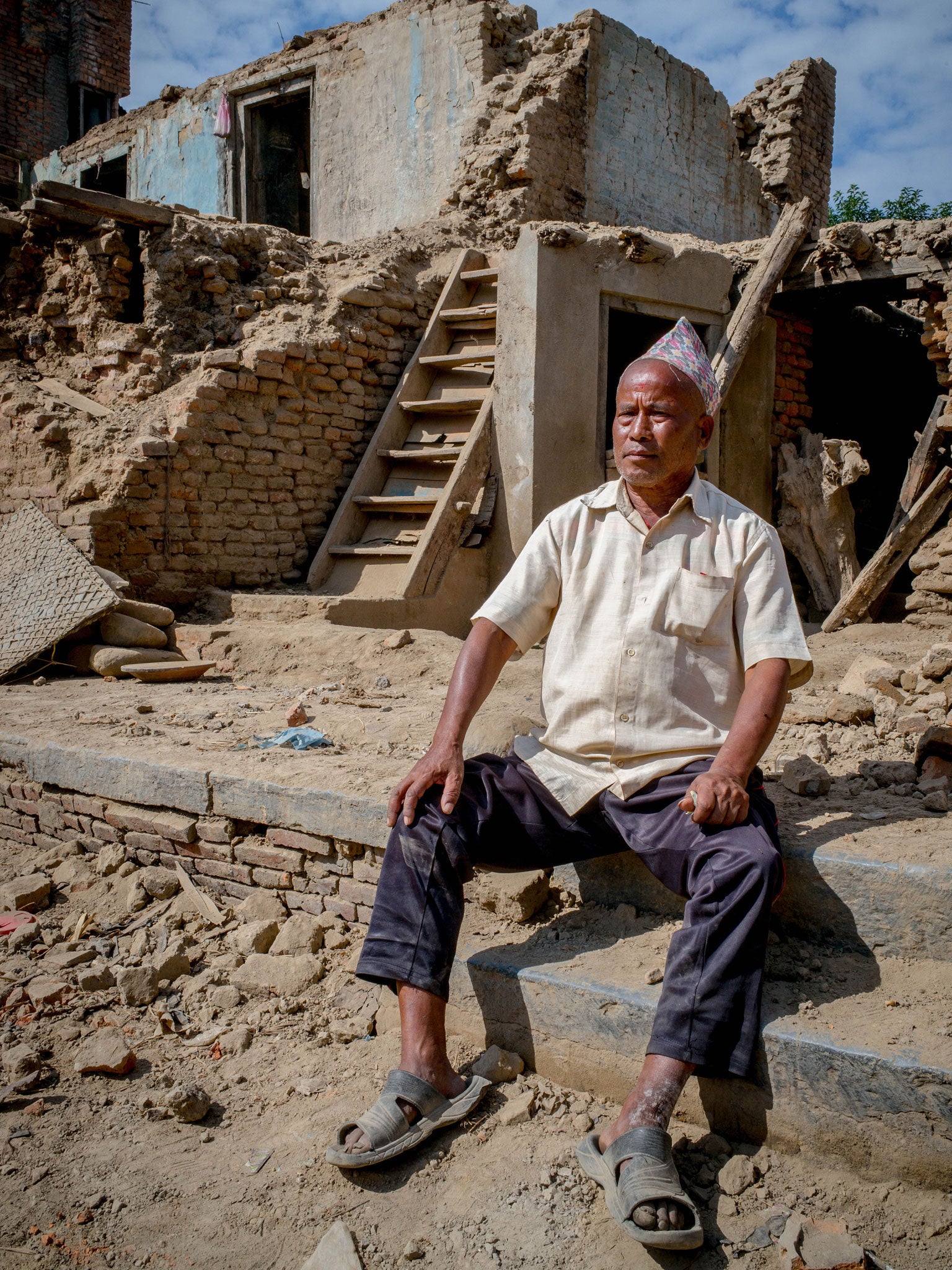 Panchamani Shakya, 66 ,sitting in a pile of rubble where his house once was – overlooking the once-magnificent, now-destroyed Machhendranath Temple in Bungamati, Nepal