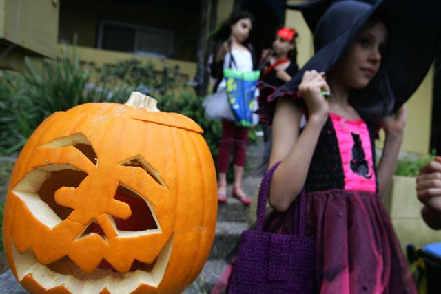 A pumpkin is seem out front of a home as children trick or treat though streets on Halloween Day