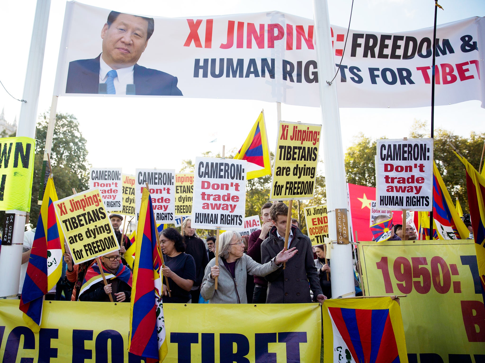 Human rights demonstrators stand beneath a protest banner bearing an image of Chinese President Xi Jinping on Parliament Square outside the Houses of Parliament, where he was giving a speech in London