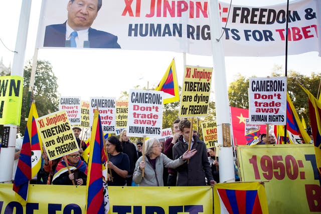 Human rights demonstrators stand beneath a protest banner bearing an image of Chinese President Xi Jinping on Parliament Square outside the Houses of Parliament, where he was giving a speech in London