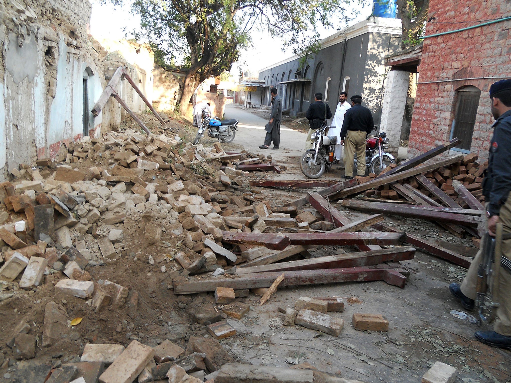 Pakistani policemen stand beside debris of collapsed houses after an earthquake in Kohat