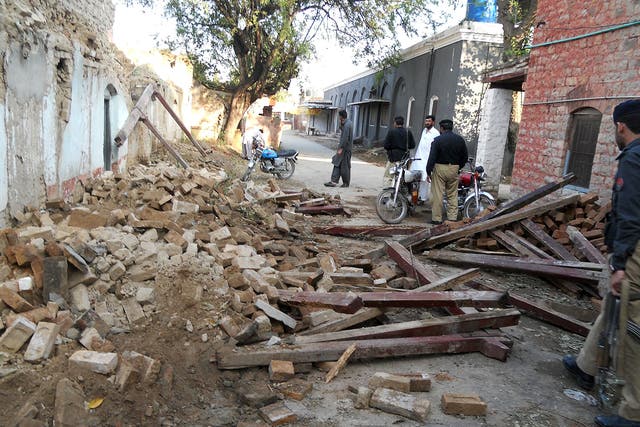 Pakistani policemen stand beside debris of collapsed houses after an earthquake in Kohat