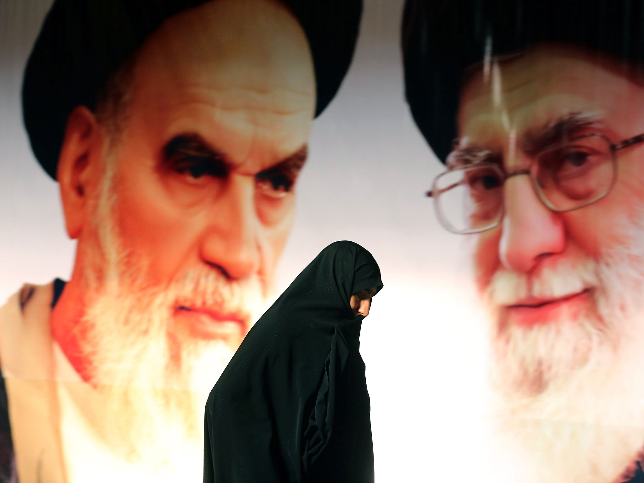 An Iranian woman walks past a poster showing supreme leader, Ayatollah Ali Khamenei (right) and the founder of Iran's Islamic Republic, Ayatollah Ruhollah Khomeini.