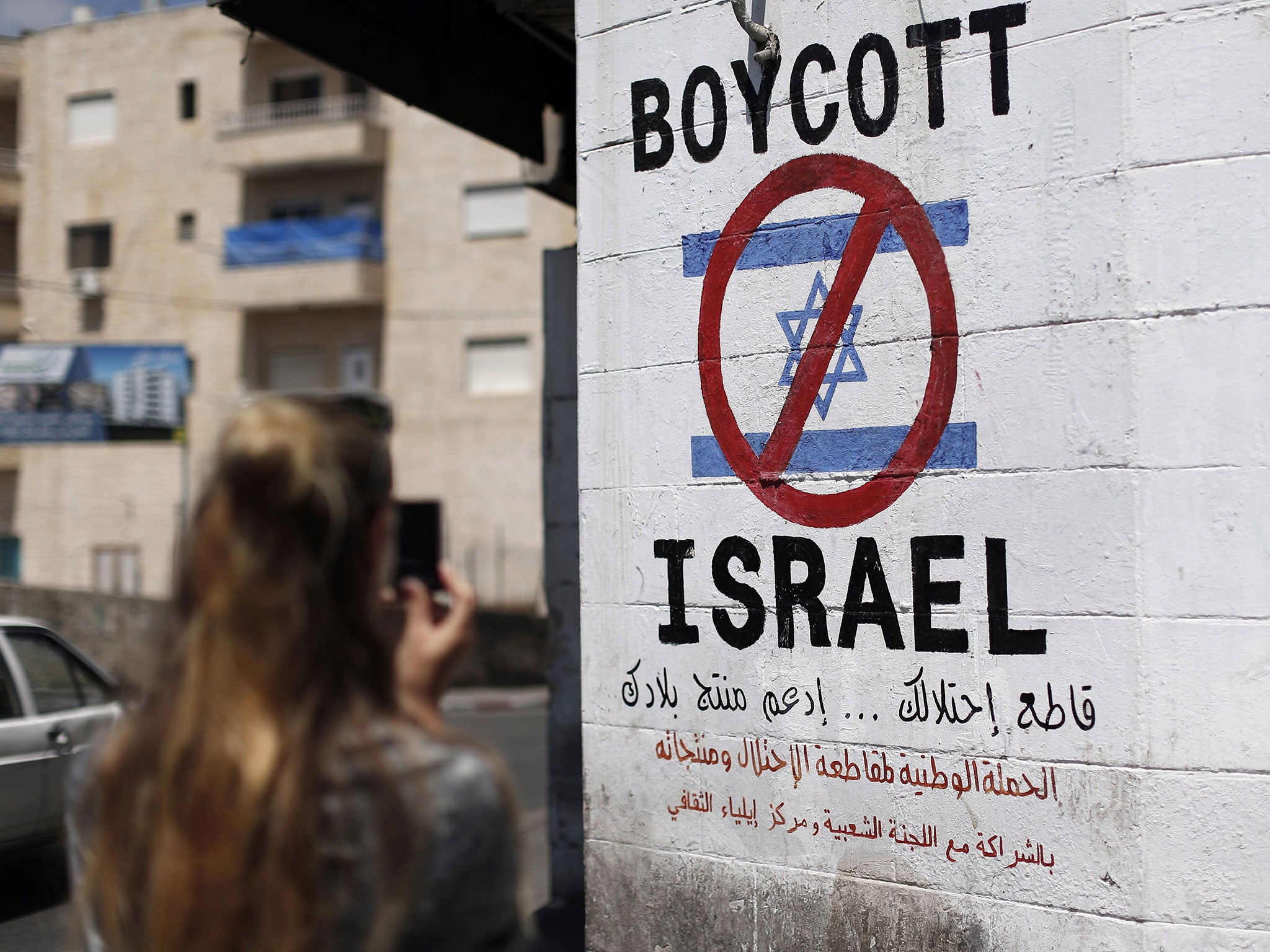 A tourist photographs a sign painted on a wall in the West Bank biblical town of Bethlehem on June 5, 2015, calling to boycott Israeli products coming from Jewish settlements.