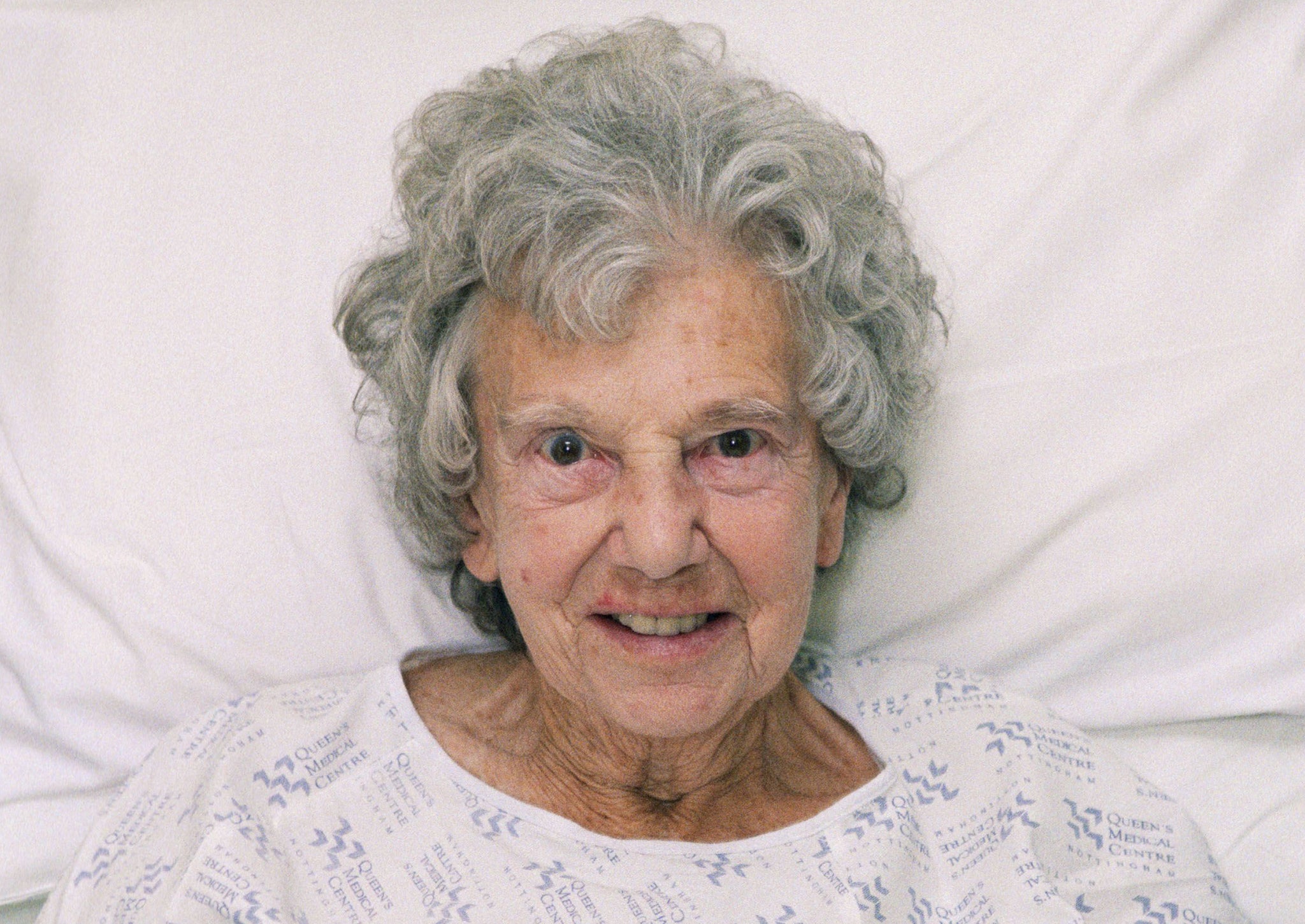 An elderly woman sitting up in a hospital bed on waits to be seen by a nurse
