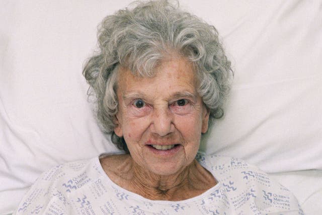An elderly woman sitting up in a hospital bed on waits to be seen by a nurse