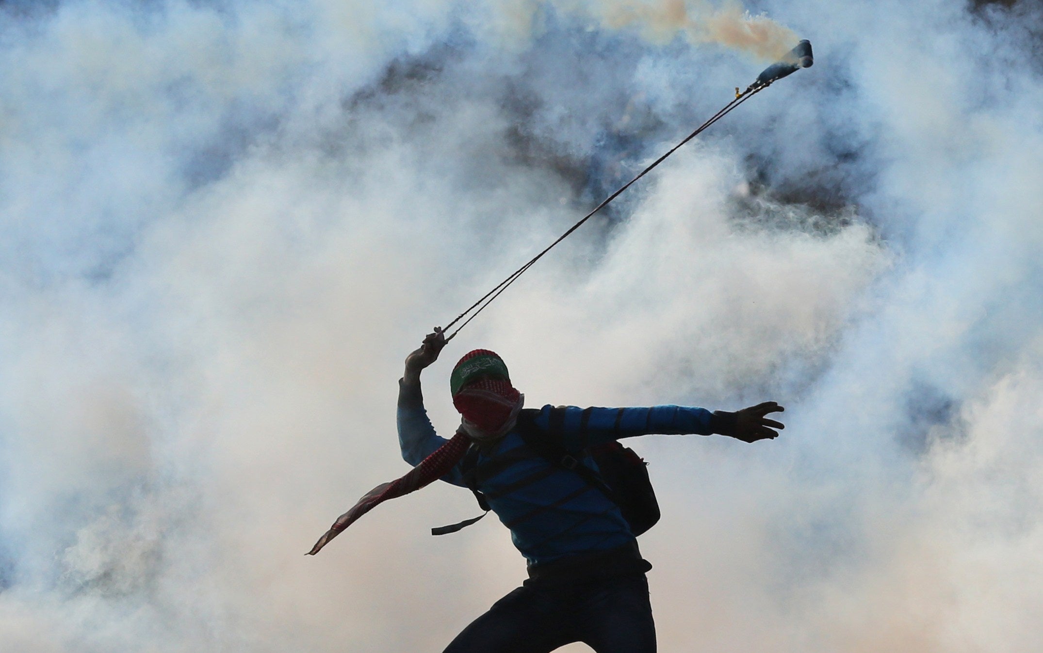 A Palestinian youth uses a slingshot to throw back a tear gas canister towards Israeli forces