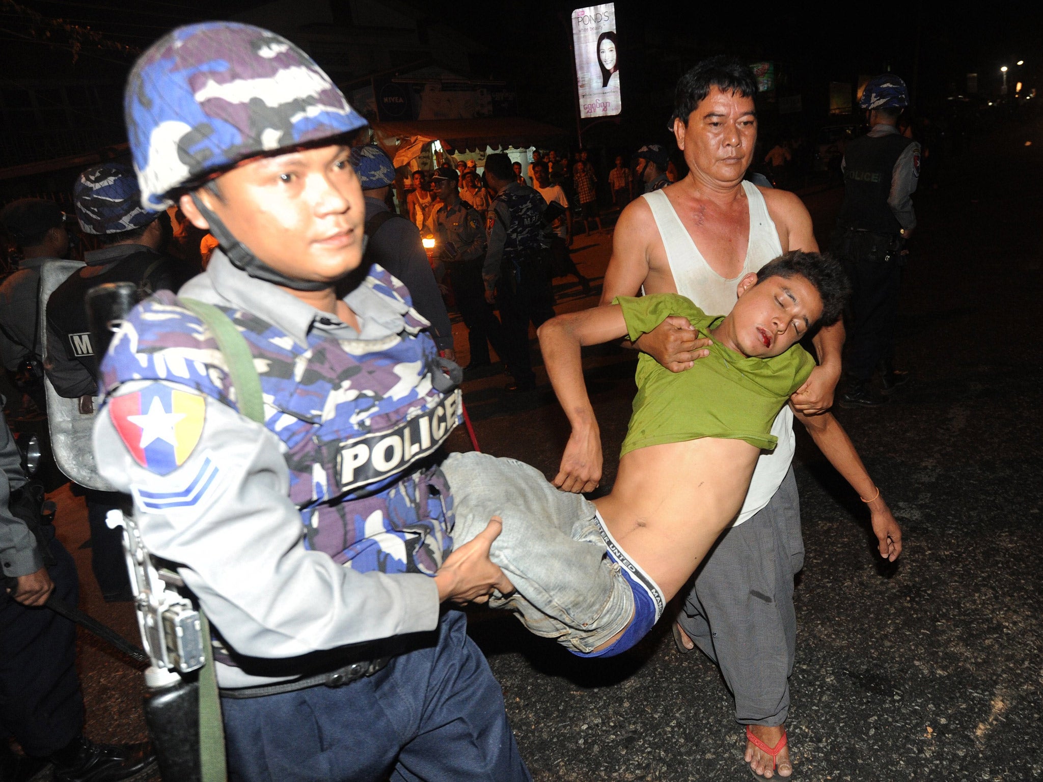 Policemen carry an injured man during anti-Muslim riots on the outskirts of Rangoon last year (Getty)