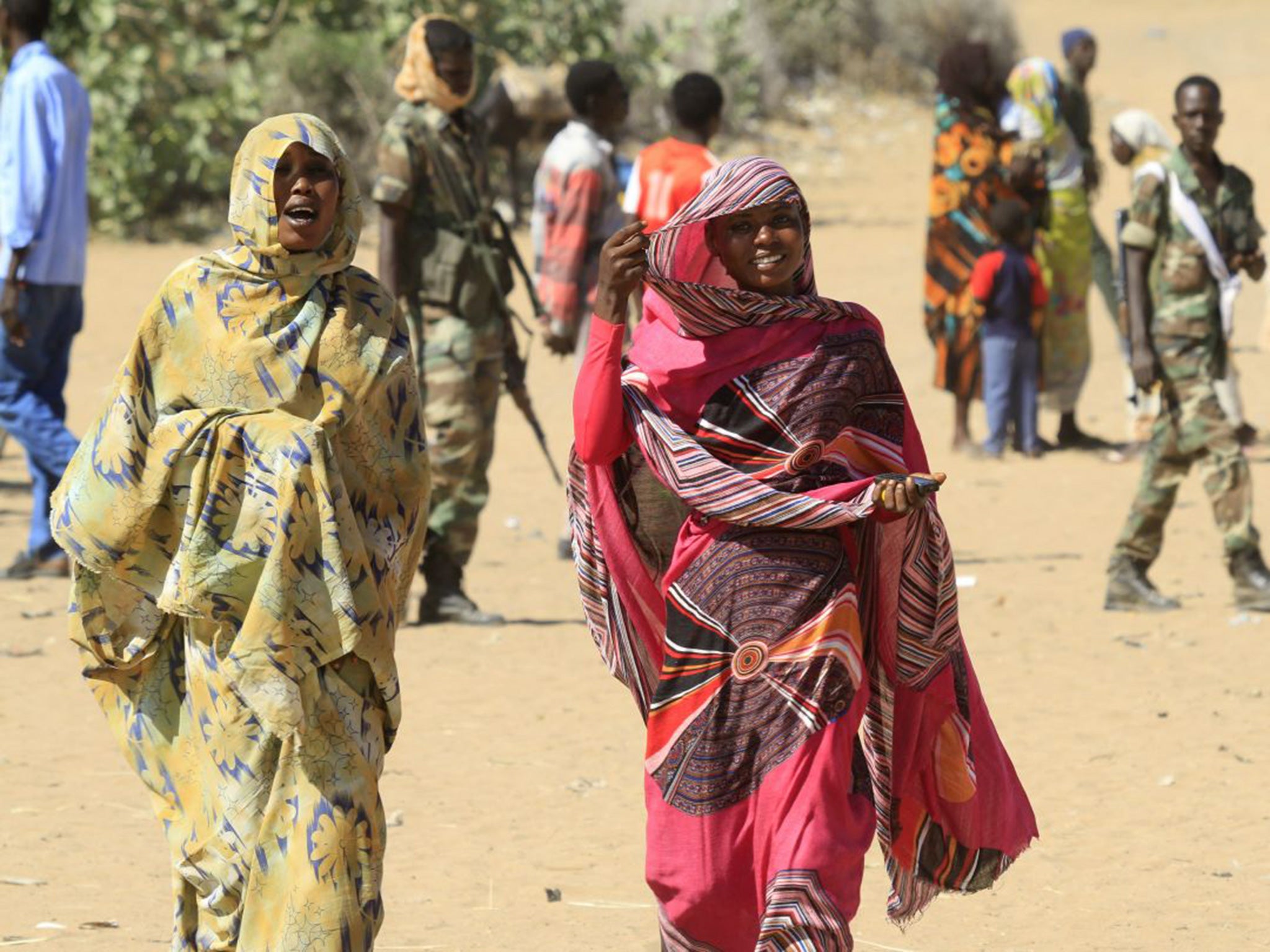 Women walk through the village of Tabit as troops stand guard