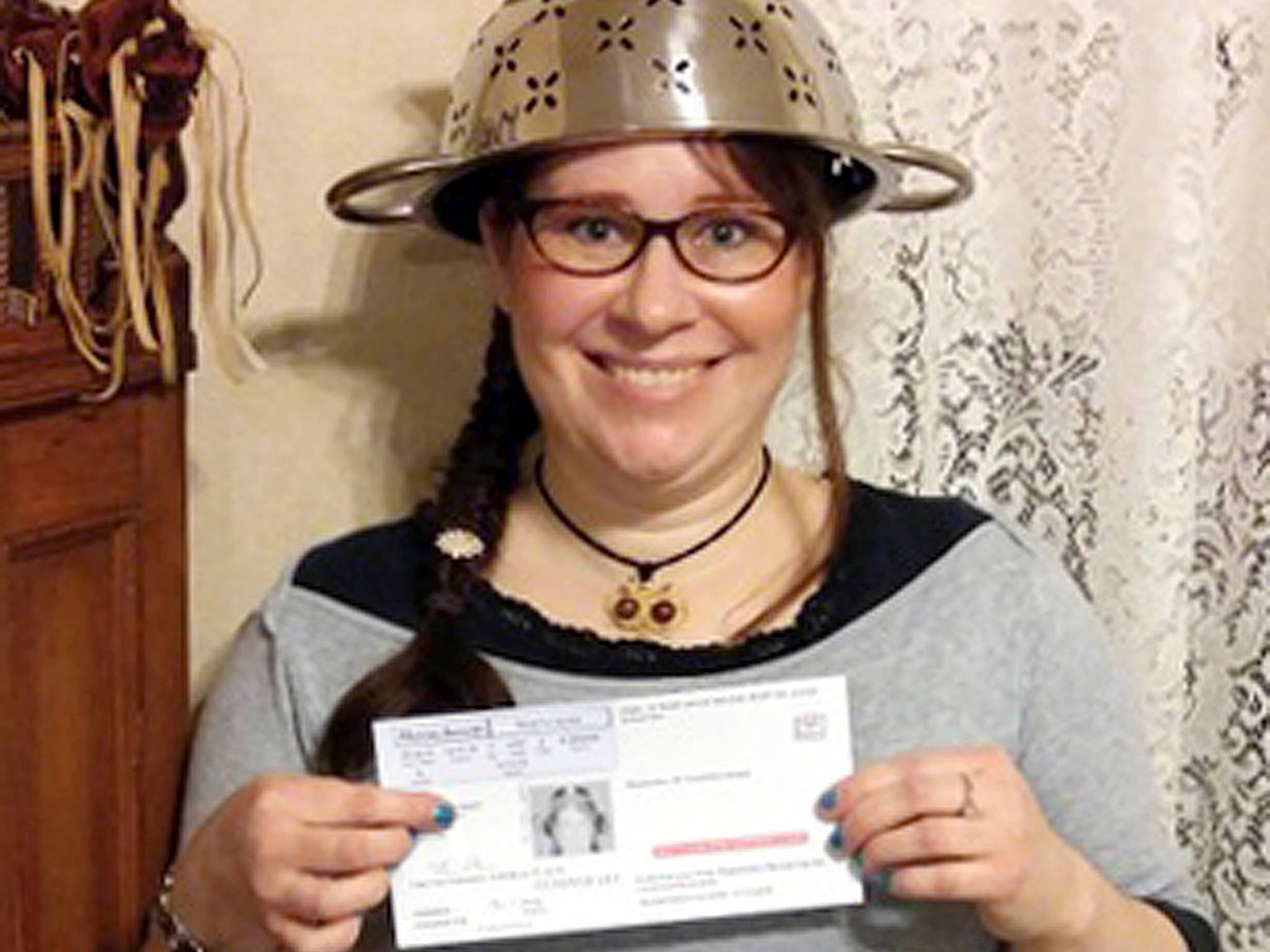 Lindsay Miller wears a spaghetti strainer to reflect her religious beliefs while holding her temporary driver license that also bears a photo of her wearing the colander.