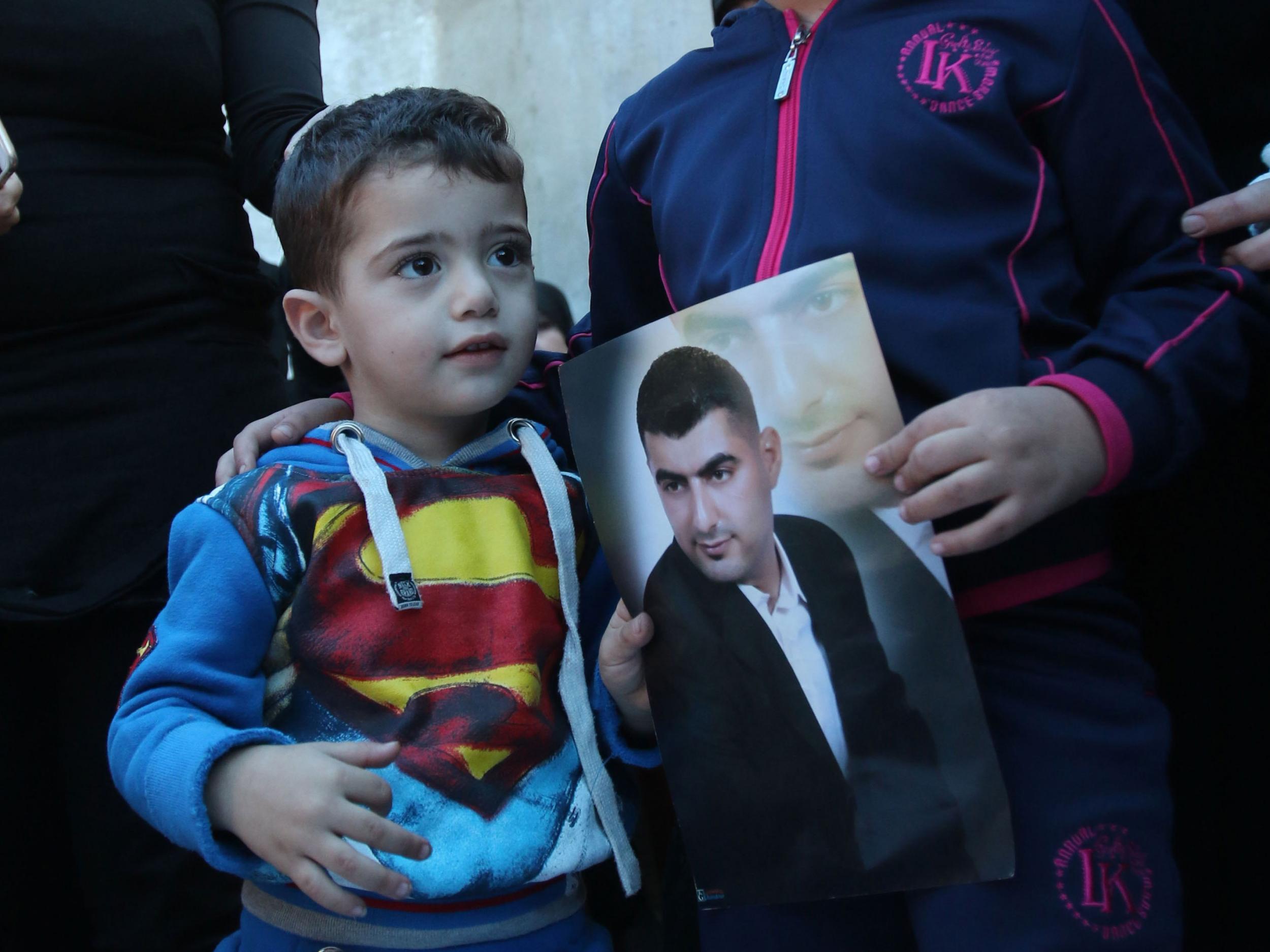 Adel Termos's son stands next to a picture of his father at his funeral