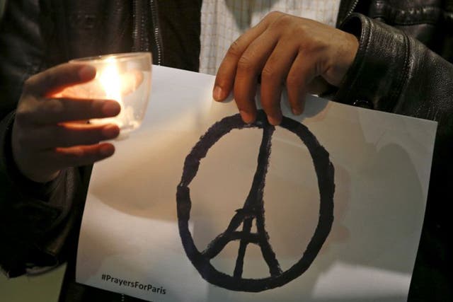 A man holds the sign of a peace symbol with the Eiffel Tower at its centre during an inter-faith vigil for the victims of the Paris attack