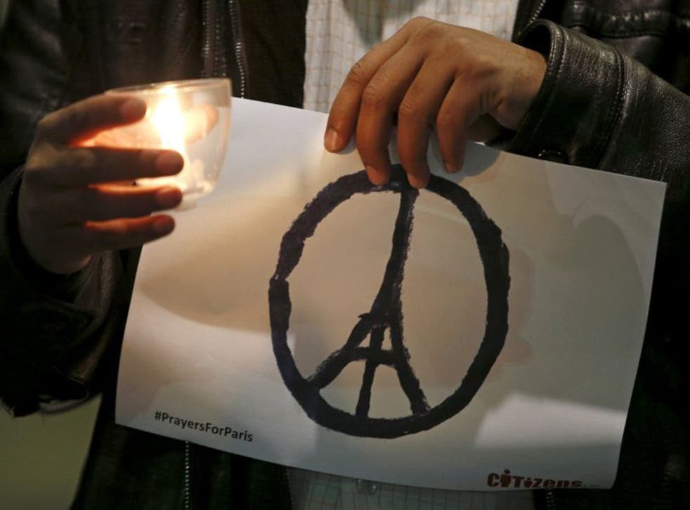 A man holds the sign of a peace symbol with the Eiffel Tower at its centre during an inter-faith vigil for the victims of the Paris attack