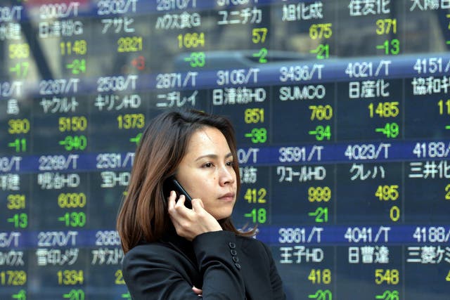A woman uses her mobile phone before a share prices board in Tokyo on May 7, 2014.