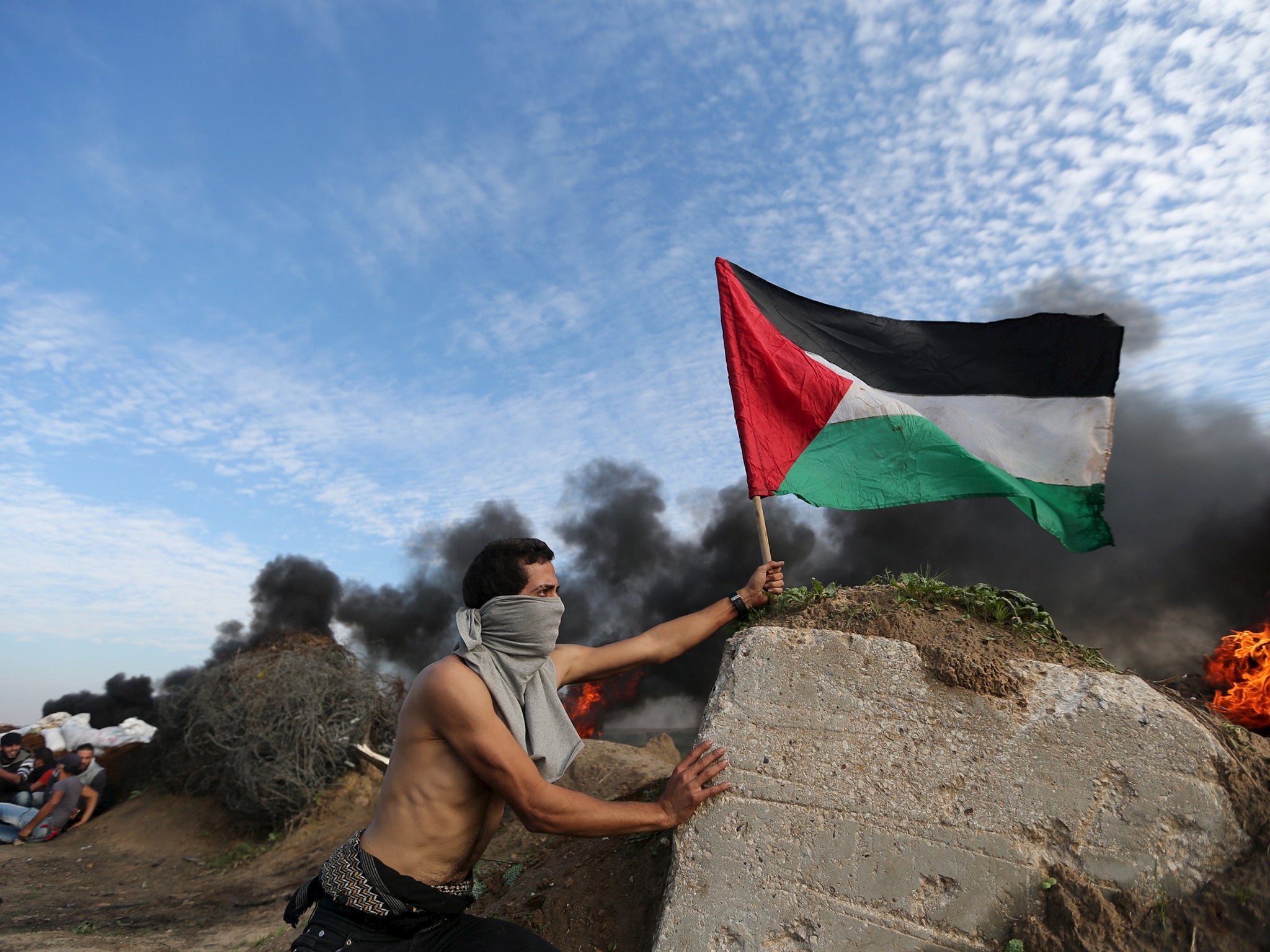 A protester places a Palestinian flag during clashes with Israeli troops near the border between Israel and Central Gaza Strip