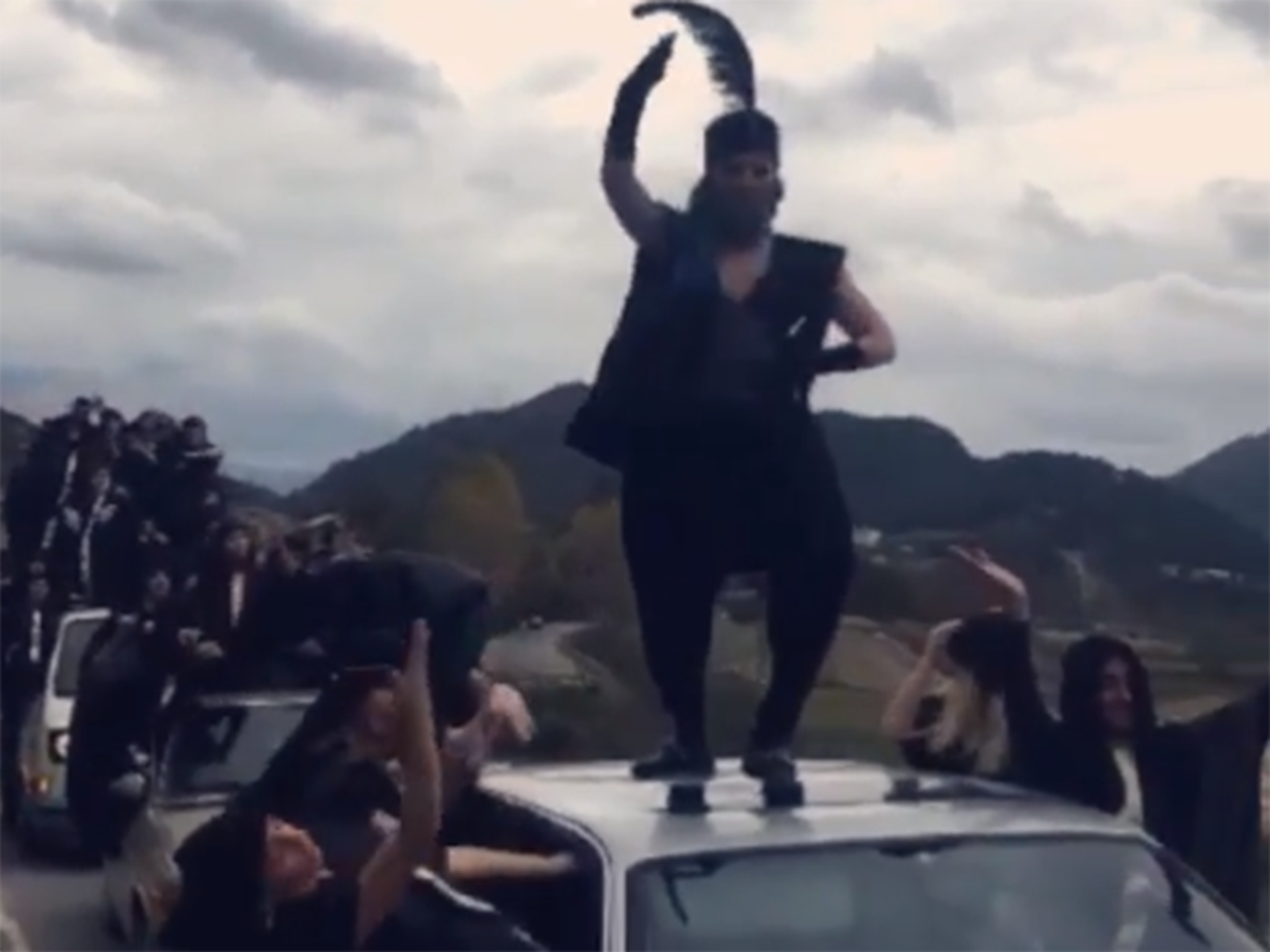 
The singer dances on top of a truck wearing a large feathered headdress 