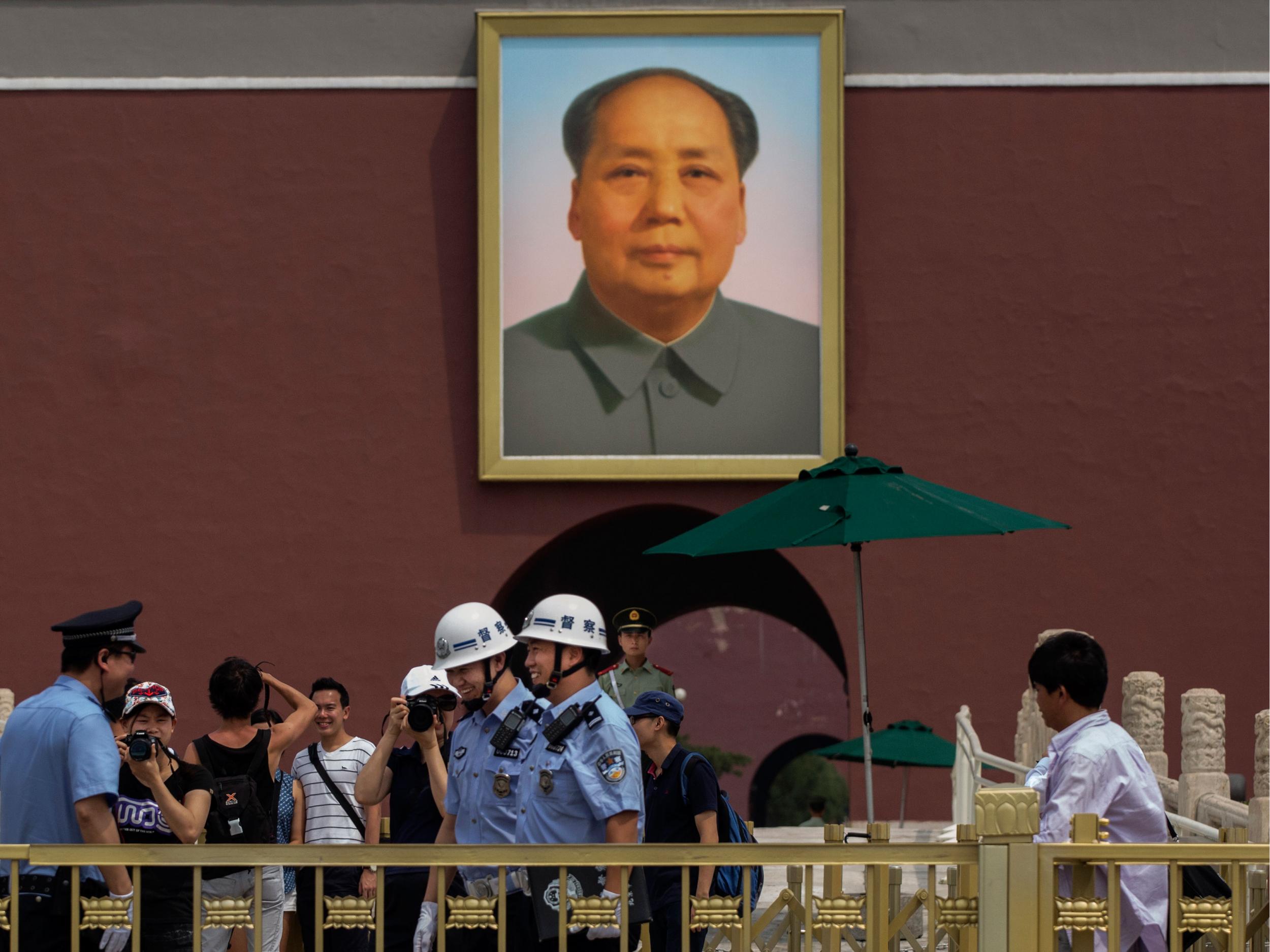 Chinese police and tourists stand underneath a picture of late leader Mao Zedong outside the Forbidden City in Tiananmen Square