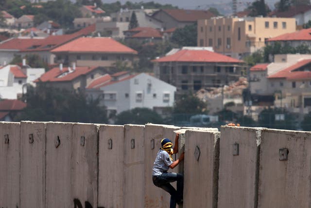A Palestinian protester climbs Israel's controversial separation barrier during clashes with Israeli security forces following a demonstration against Israeli settlements and its separation wall, in the West Bank village of Nilin near the Jewish settlement of Hashmonaim (background), on 14 June, 2013