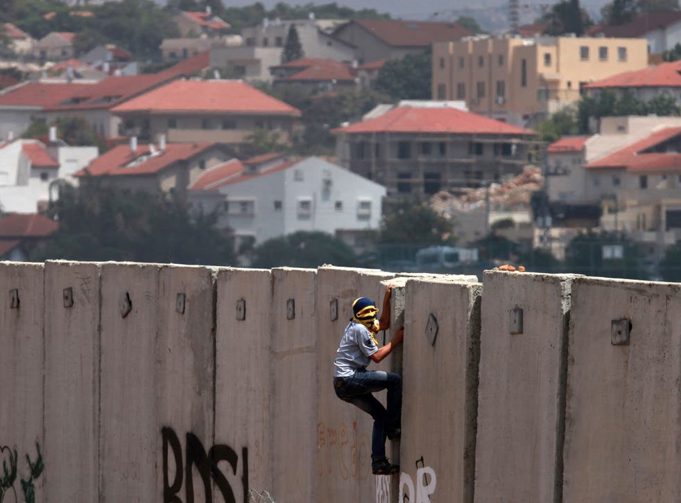 A Palestinian protester climbs Israel's controversial separation barrier during clashes with Israeli security forces following a demonstration against Israeli settlements and its separation wall, in the West Bank village of Nilin near the Jewish settlement of Hashmonaim (background), on 14 June, 2013