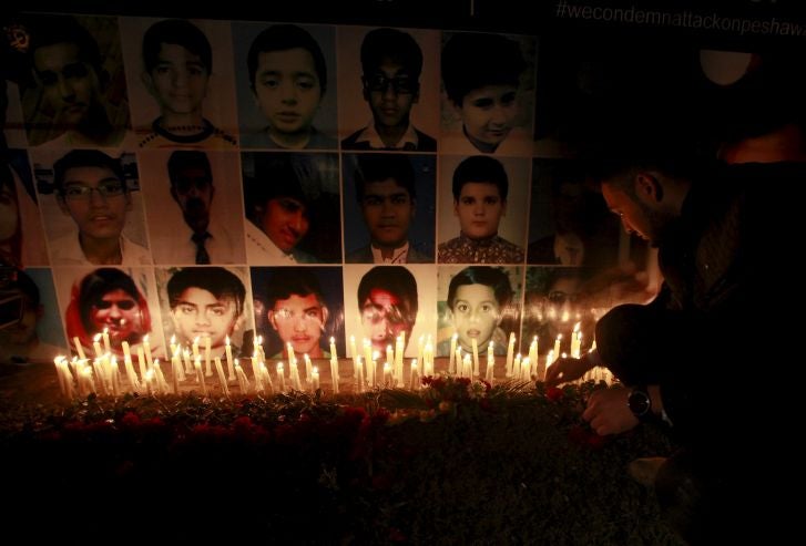 A man places a rose after lighting candles in front of portraits of the victims of the Taliban attack on the Army Public School in Peshawar