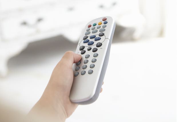 Young girl holding television remote control in bedroom
