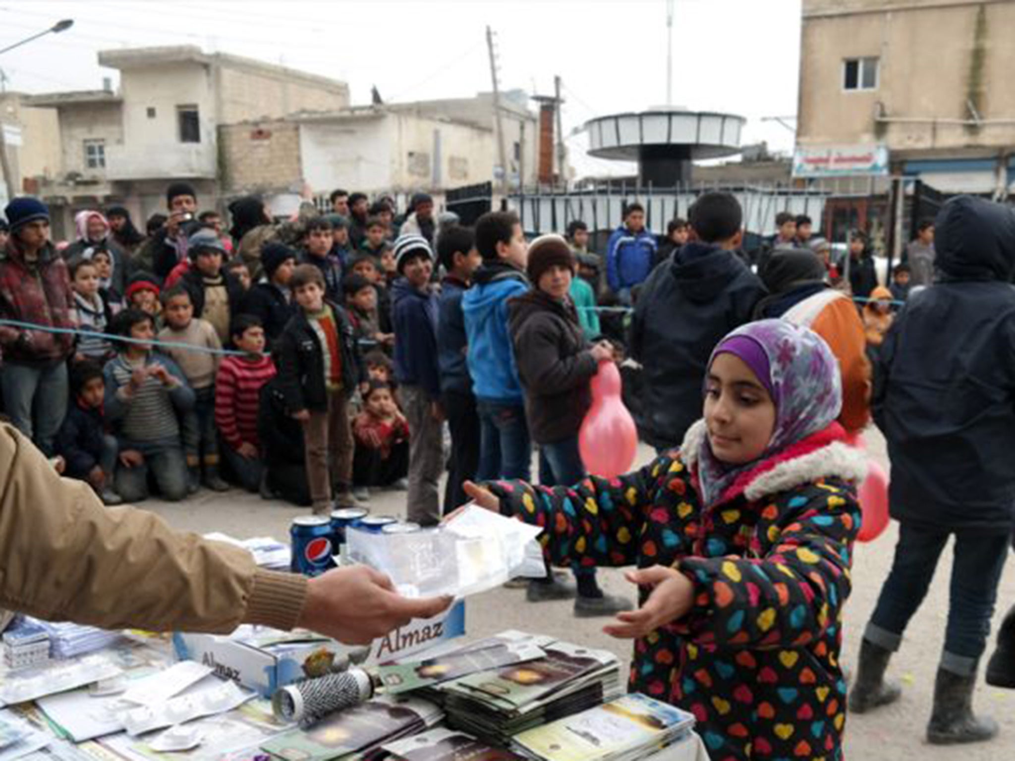 An Isis militant, left, distributes biscuits, along with religious pamphlets to a Syrian young girl, right, during a street preaching event in Raqqa