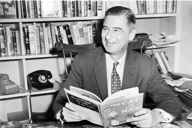 Ted Geisel (Dr Seuss) seated at desk covered with his uniquely humorous children's books