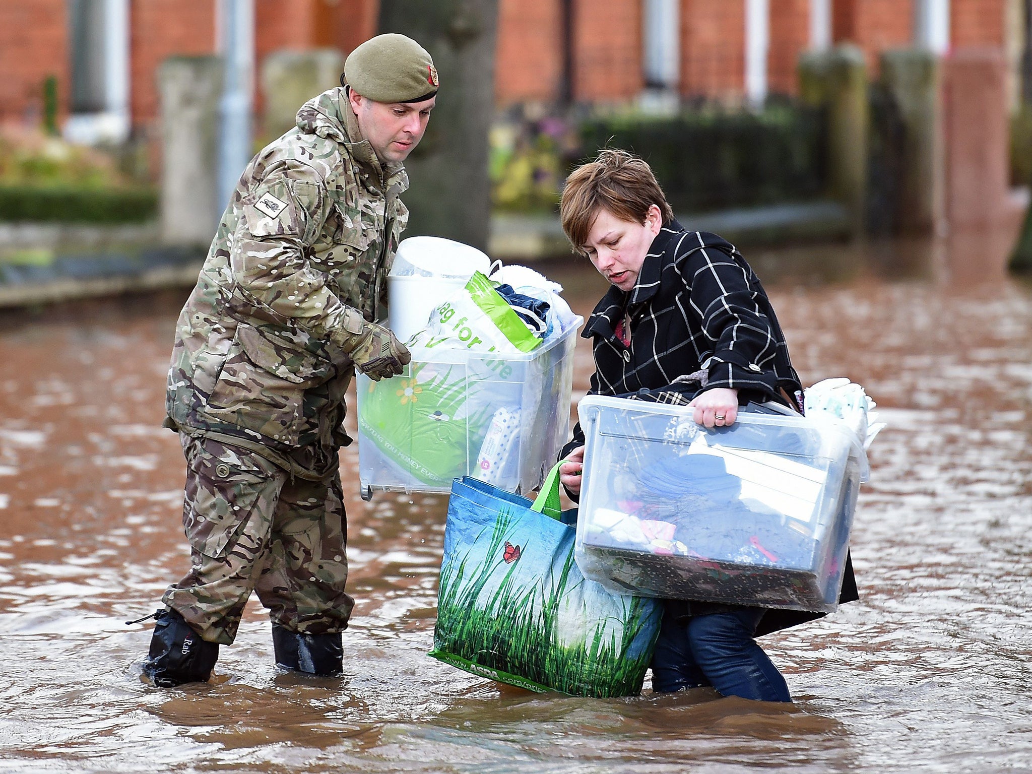 A member of the British army helps a woman carry belongings through a flooded street in Carlisle