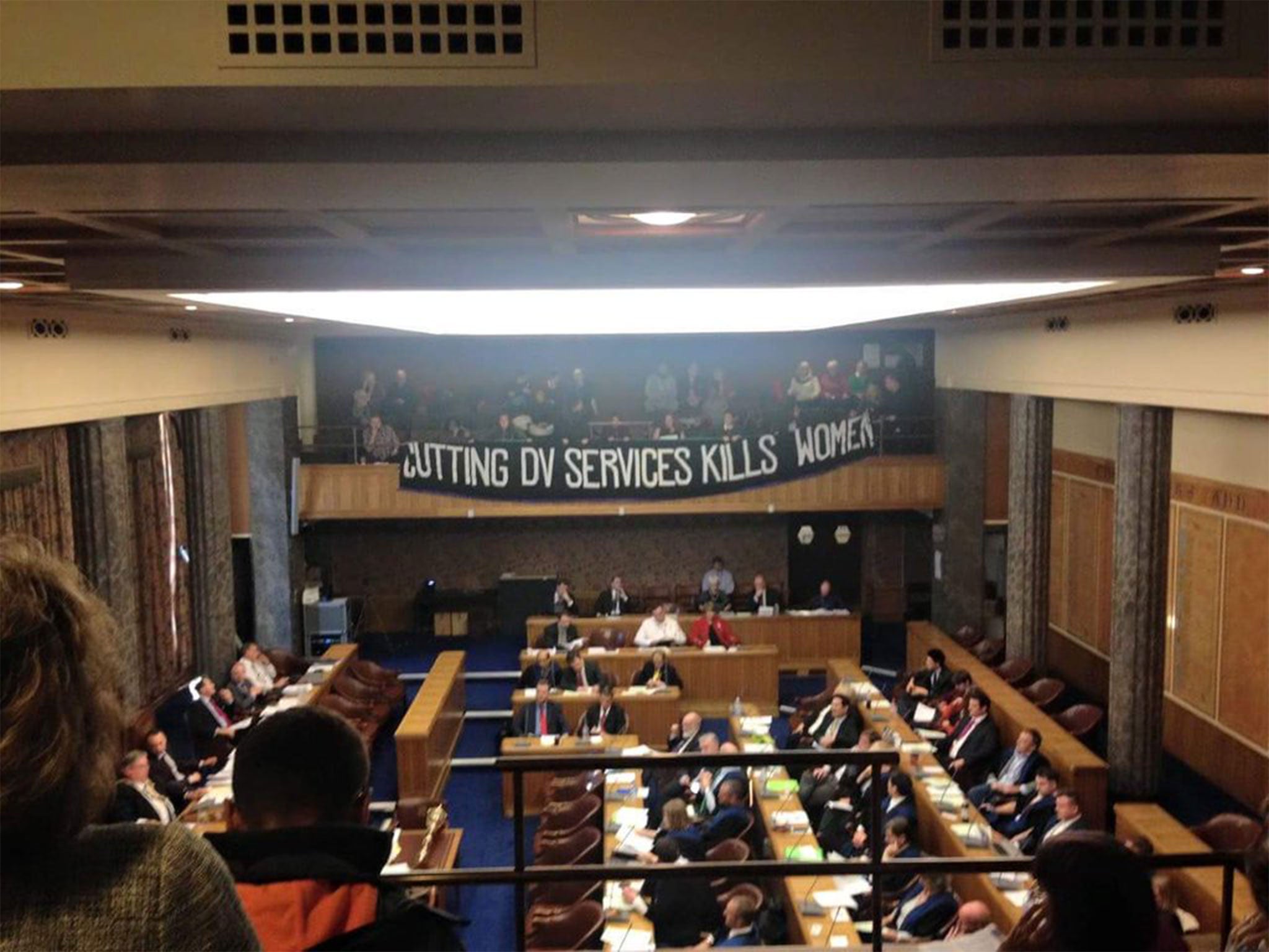 Sisters Uncut unfurl their banner over the council chamber