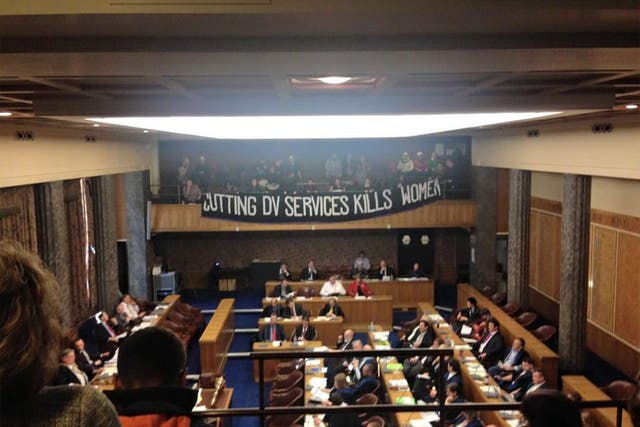 Sisters Uncut unfurl their banner over the council chamber