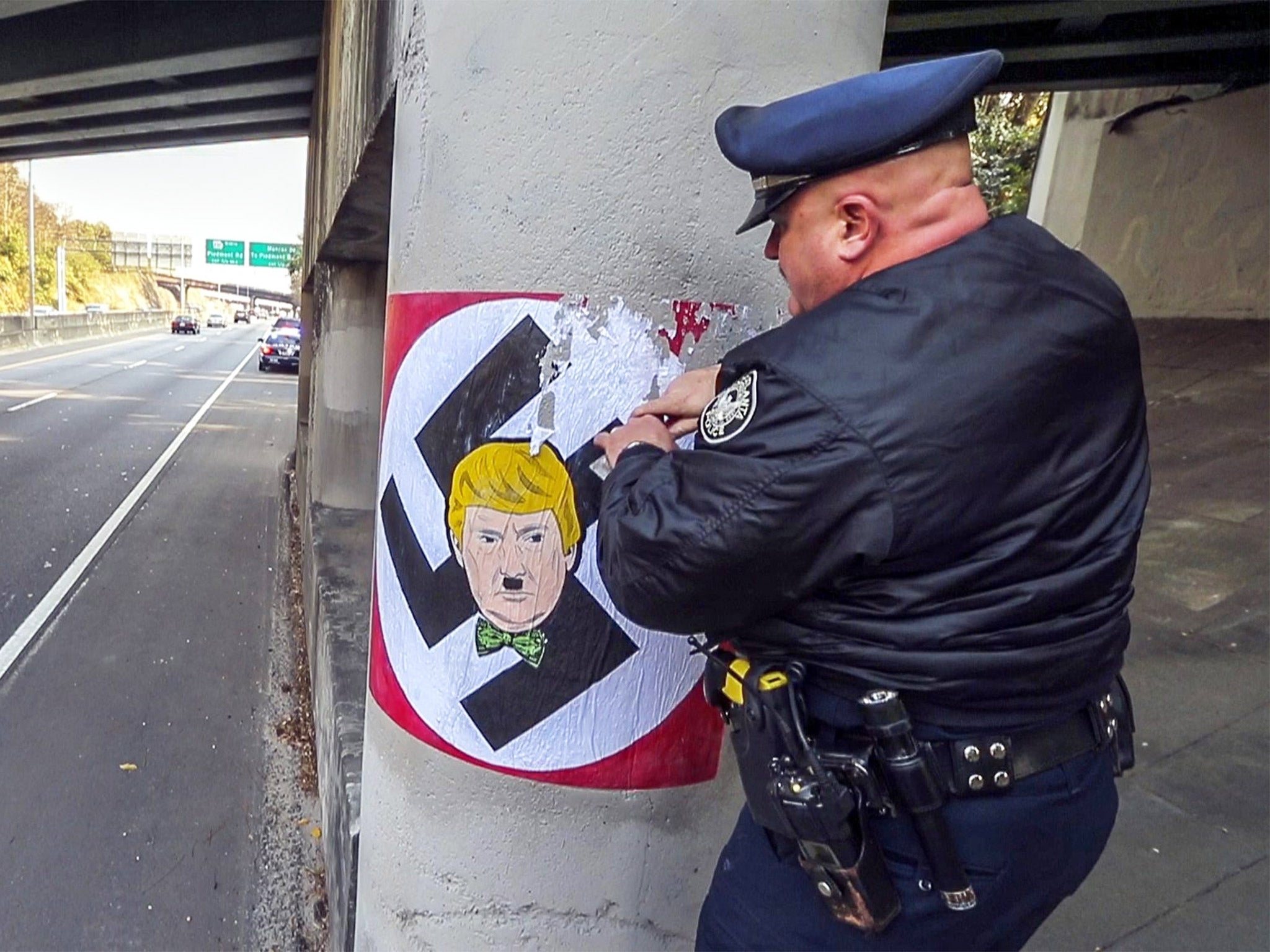 An Atlanta police officer removes graffiti depicting Donald Trump as Adolf Hitler