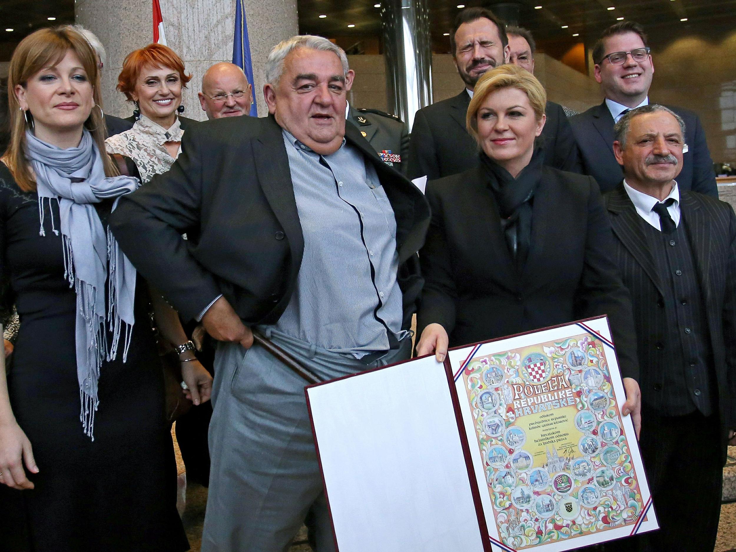 Croatia's leading rights group chief Ivan Zvonimir Cicak's looks down after his trousers fell down while posing for a photo with Croatian President Kolinda Grabar-Kitarovic