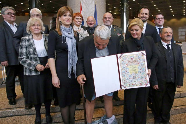 Croatia's leading rights group chief Ivan Zvonimir Cicak's looks down after his trousers fell down while posing for a photo with Croatian President Kolinda Grabar-Kitarovic