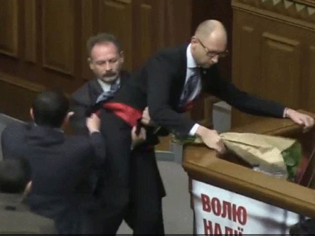 MP Oleh Barna is captured trying to lift Arseniy Yatsenyuk, the prime minister, away from his podium during the annual statement