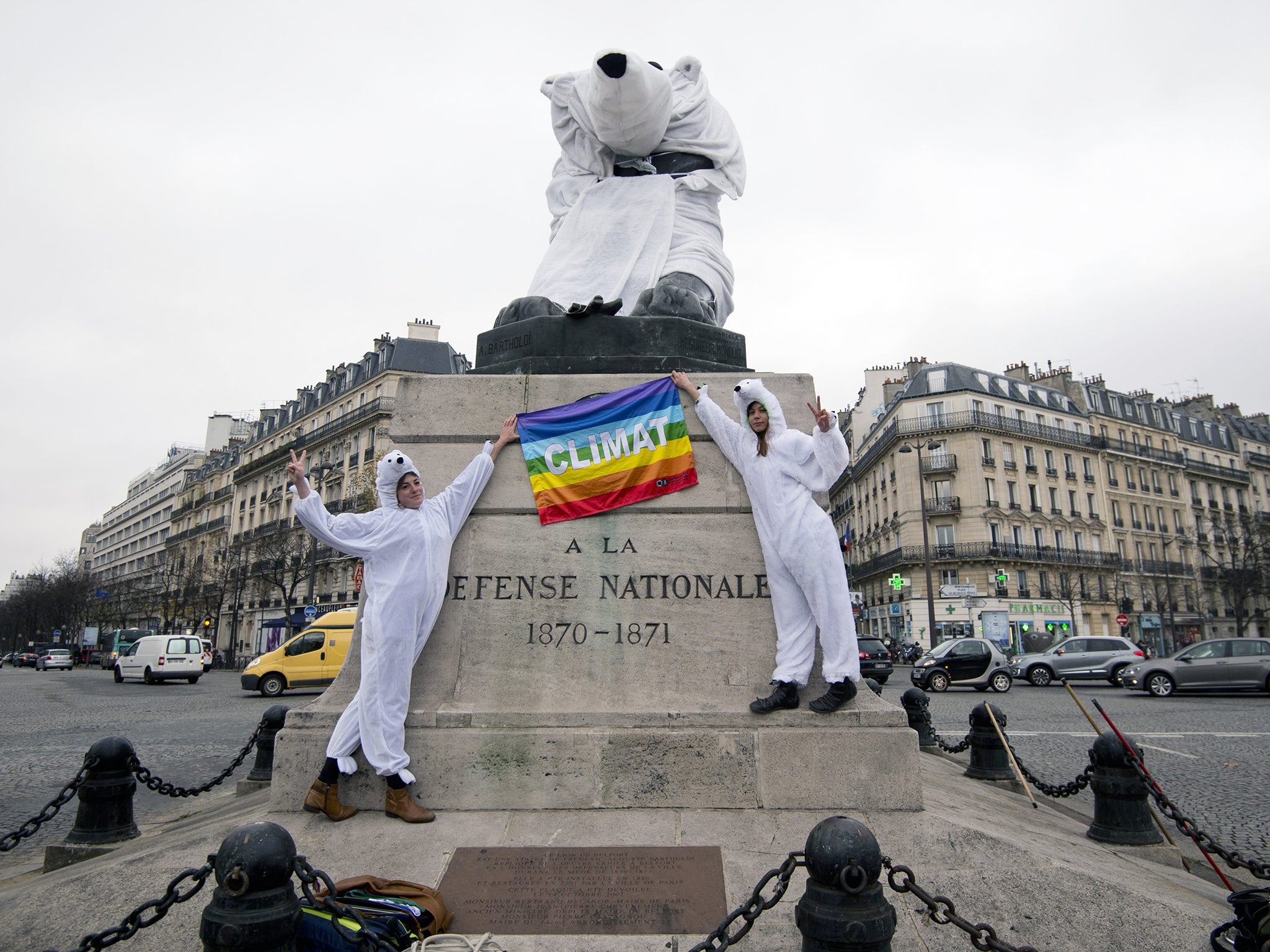 Two women dressed as polar bear hold a peace flag with an inscription reading "Climat" as the gestures a victory sign in front of the "Lion of Belfort" statue, also dressed as a polar bear, on the Denfert-Rochereau place in Paris.