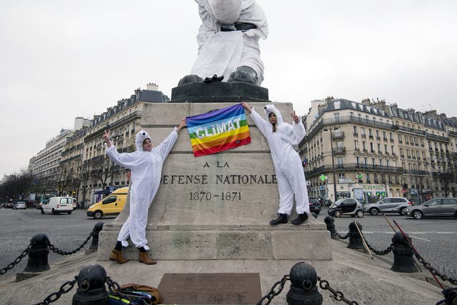 Two women dressed as polar bear hold a peace flag with an inscription reading "Climat" as the gestures a victory sign in front of the "Lion of Belfort" statue, also dressed as a polar bear, on the Denfert-Rochereau place in Paris.