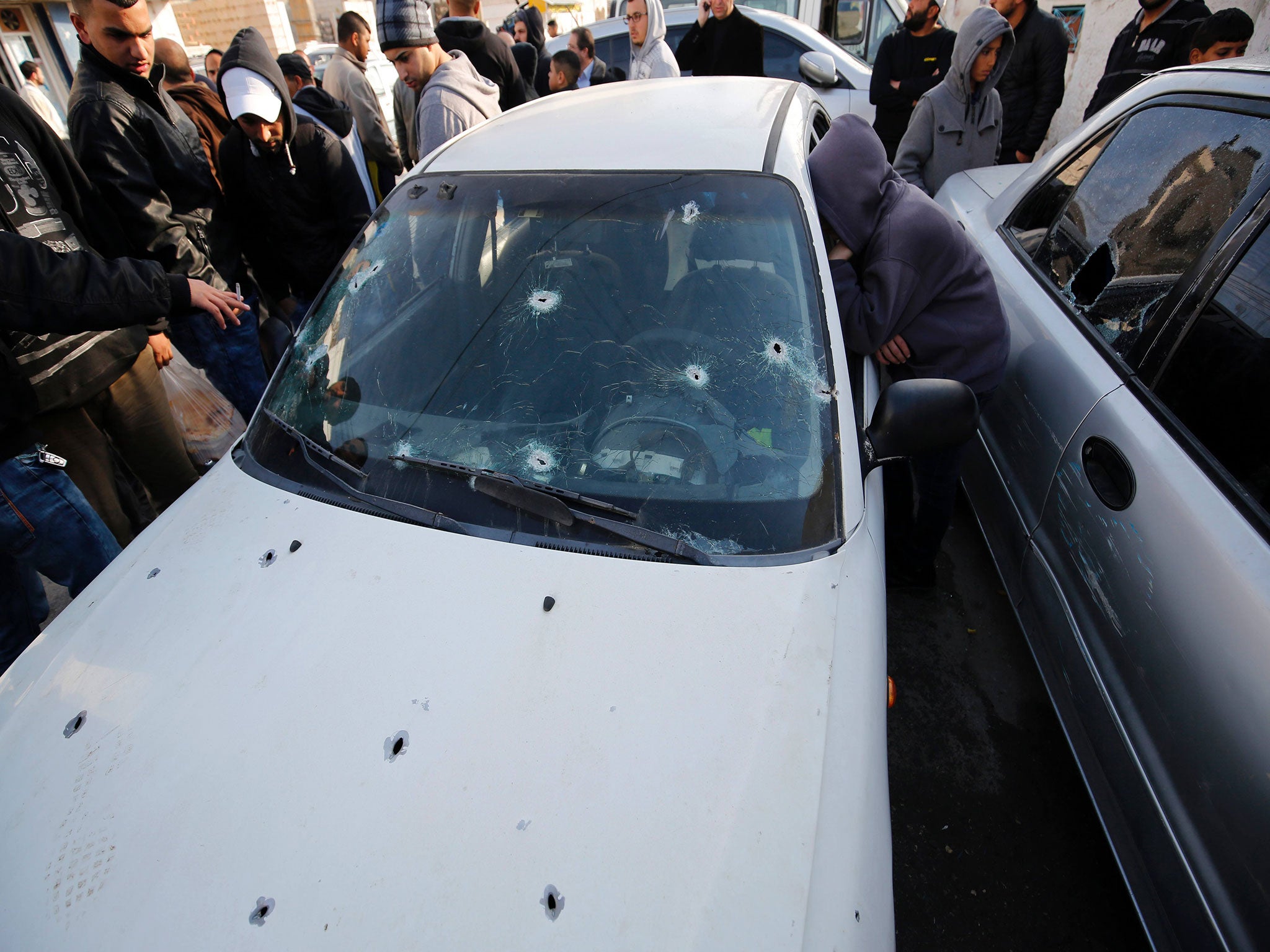 Palestinians stand next to a car, used by Palestinians in an attempted ramming attack against Israeli soldiers, in the Qalandia refugee camp near the West Bank city of Ramallah on December 16, 2015.
