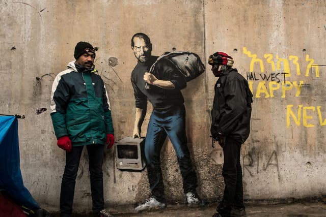 Two men stand next to Banksy's Steve Jobs mural in the Calais migrant camp