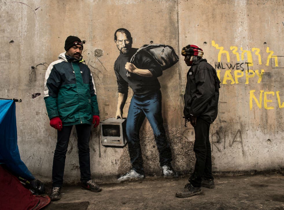 Two men stand next to Banksy's Steve Jobs mural in the Calais migrant camp