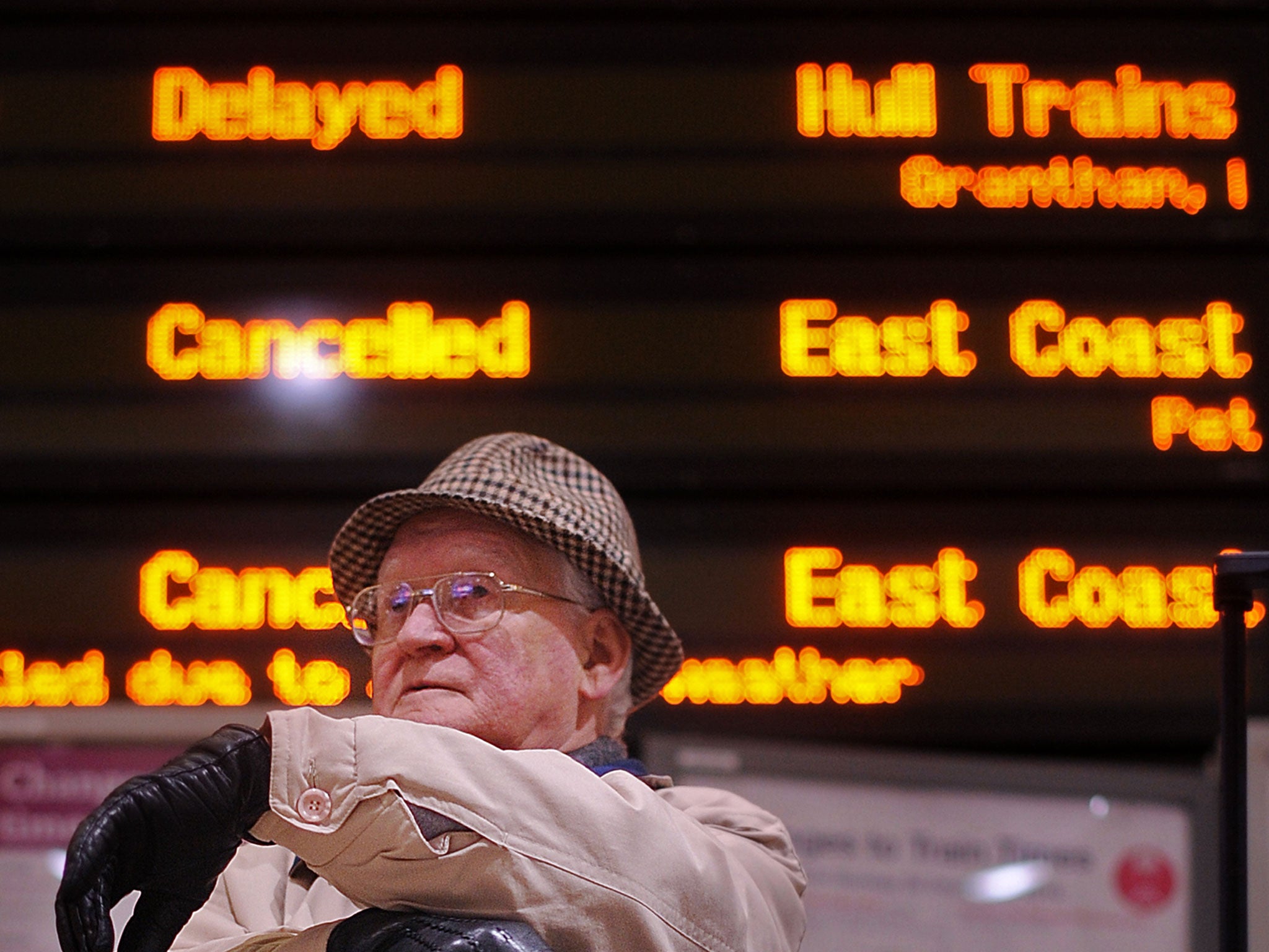 A passenger sits underneath an electronic information board showing cancelled and delayed trains, at Kings Cross train station in London