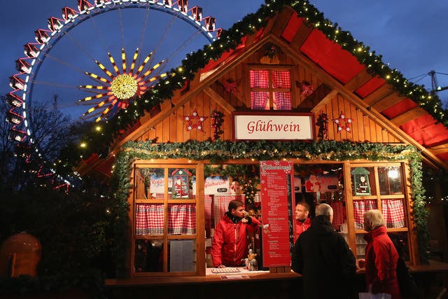 Visitors stop at a stall selling glühwein next to an illuminated ferris wheel at the Christmas market at Alexanderplatz