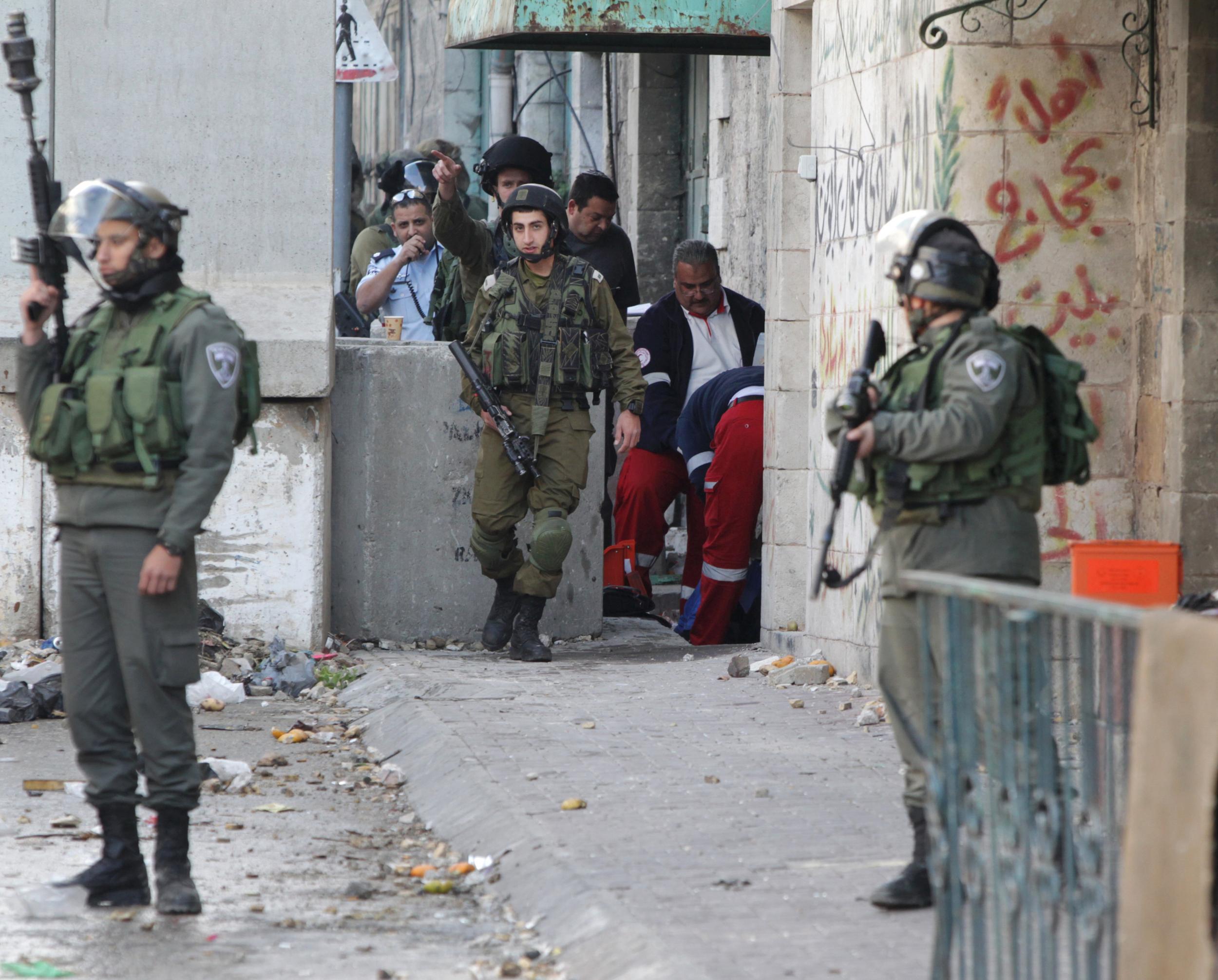 Israeli troops stand guard as medics treat a Palestinian woman hit with rubber attacks during an attempted attack on the army in Hebron in the West Bank
