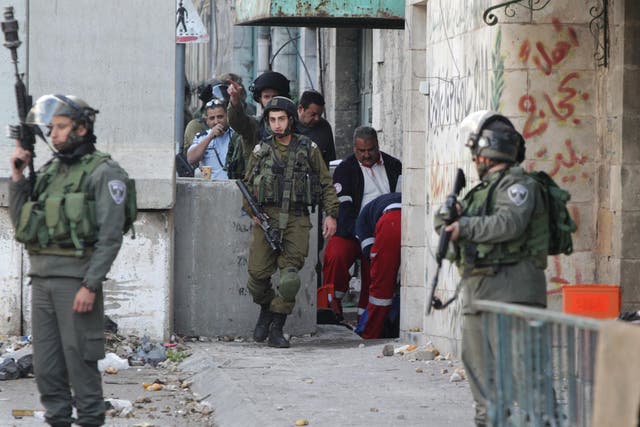 Israeli troops stand guard as medics treat a Palestinian woman hit with rubber attacks during an attempted attack on the army in Hebron in the West Bank