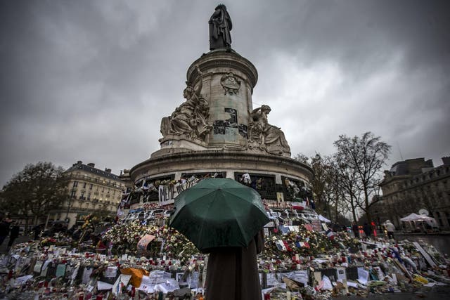 A pedestrian with an umbrella pauses in front of the memorial of candles and flowers for the victims of the 13 November Paris