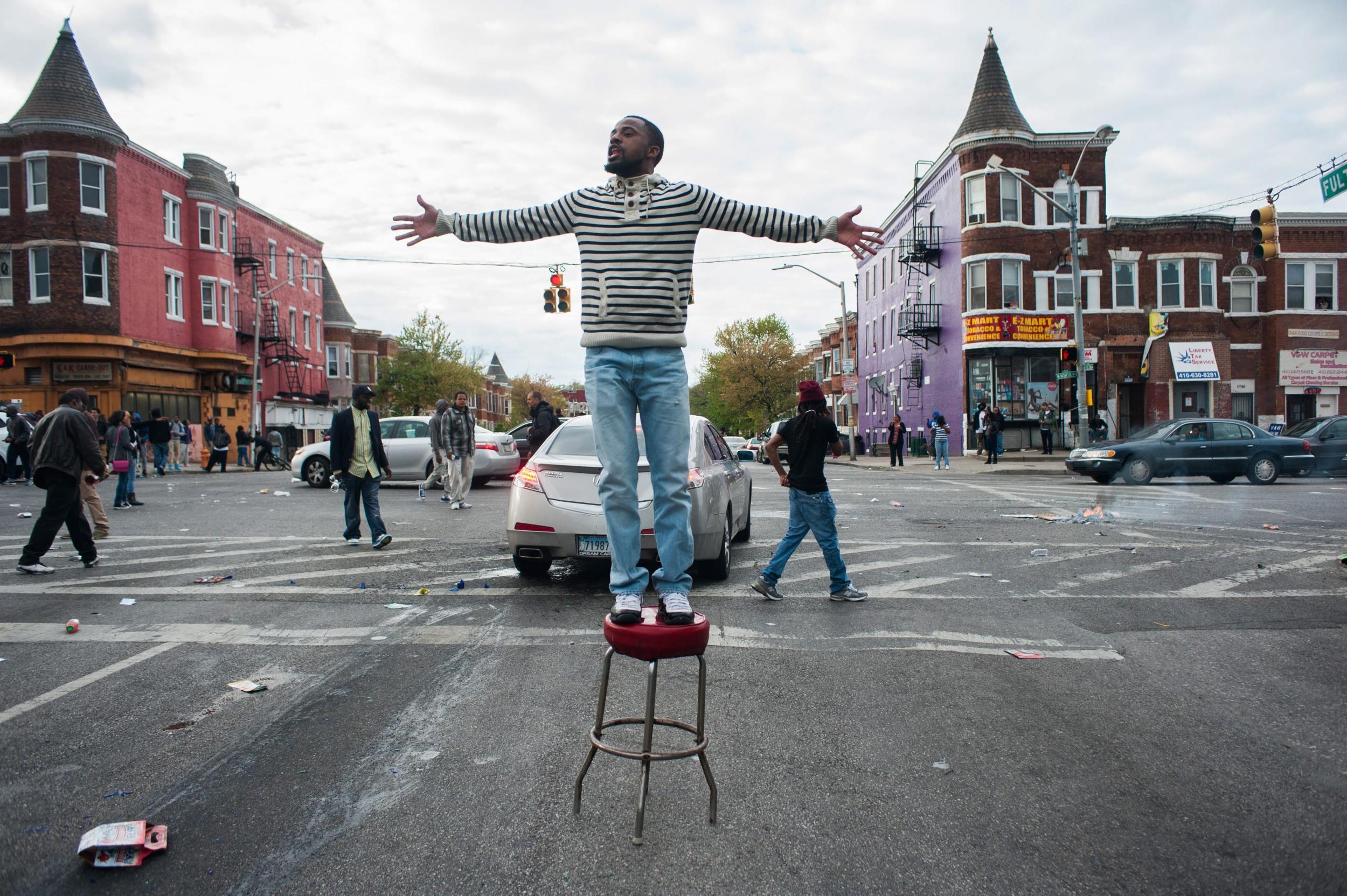 A protestor stands on a stool by looted businesses on North Avenue and Fulton Street during a protest for the death of Freddie Gray in Baltimore, Maryland, USA